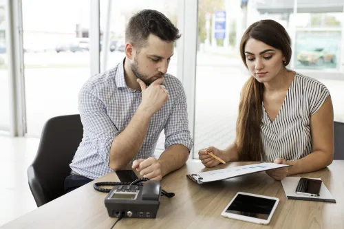 Dois colegas de trabalho analisam gráficos financeiros num escritório moderno, com tablet, telemóveis e telefone fixo sobre a mesa. Imagem que representa consultoria financeira e planeamento de crédito.